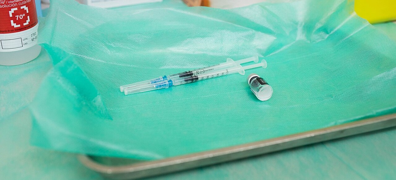 Dos jeringuillas cargadas y un vial de vacuna sobre una bandeja con paño verde en un centro de salud